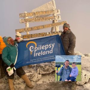 Mark on top of Kilimanjaro with Epilepsy Ireland flag and a picture of Mark and Ciarán inset