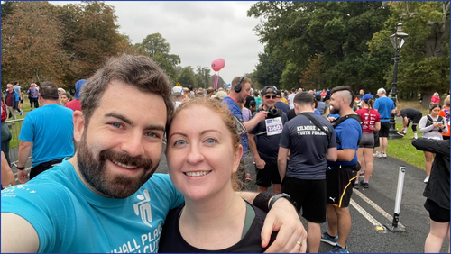 A man and a woman smiling at the camera against a backdrop of runners