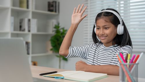 Child at Laptop with colouring pencils and her hand raised.