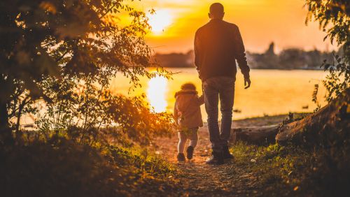 Father and child walking towards sunset 