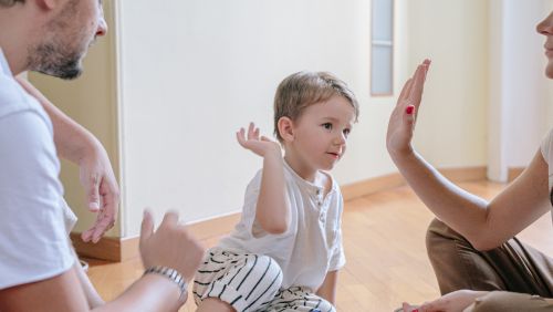 Child high fiving mother with father looking on.