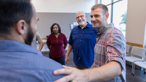 Man smiling with hand on another man's shoulder with people in the background smiling