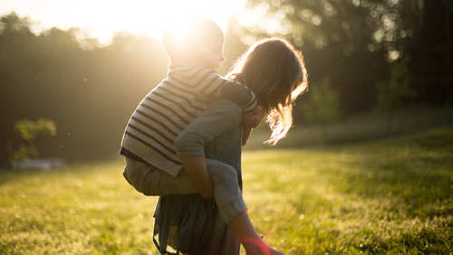 A girl giving a boy a piggyback in the sunshine
