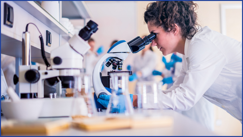 Girl looking into a microscope while wearing a lab coat