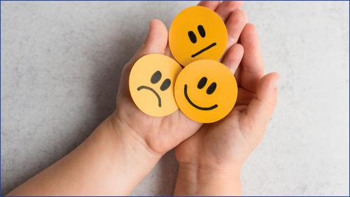 Person holding emoji faces depicting sad, happy & indifferent feelings