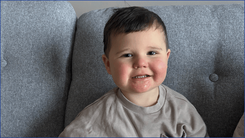 Toddler wearing a grey shirt sitting on a grey couch