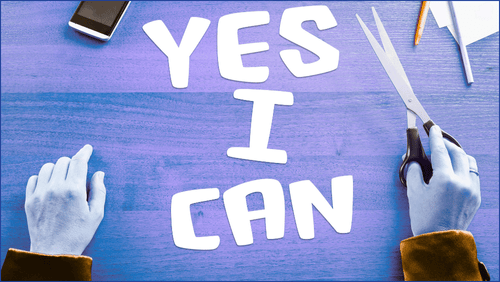 Person holding scissors who has cut out letters saying YES I CAN