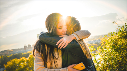 Two woman hugging with sun setting in background