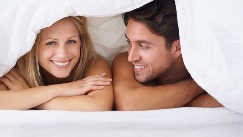 smiling man and woman under the covers of a bed.