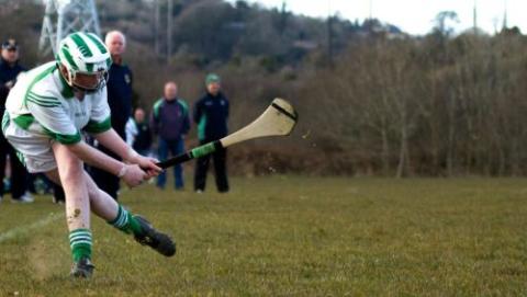 Young man playing hurling with people watching in the background